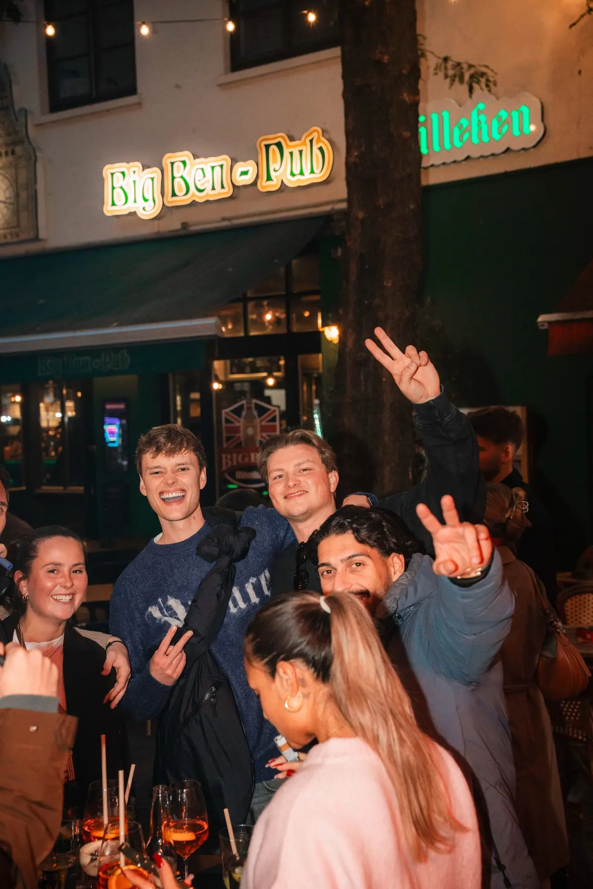 Eine Gruppe junger Leute feiert abends draußen vor der Kneipe