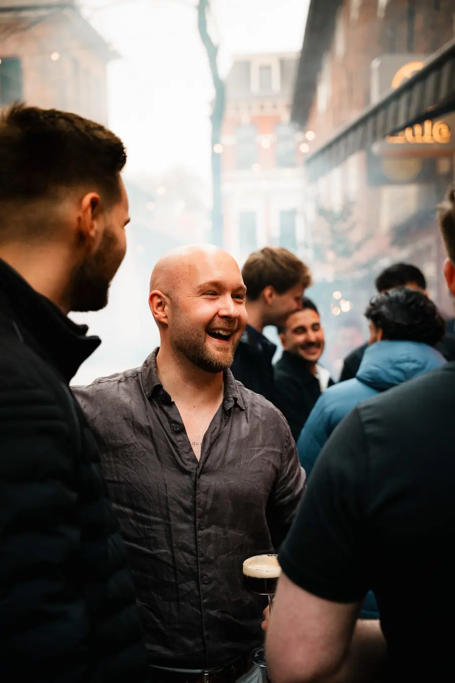 Ein Gast lacht mit einem dunklen Bier in der Hand vor der Eule